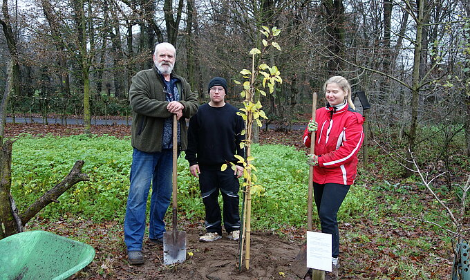  Hartmut Wunderlich, Liam Bell und Lilly Malkus stehen neben dem frisch gepflanzten Baum.